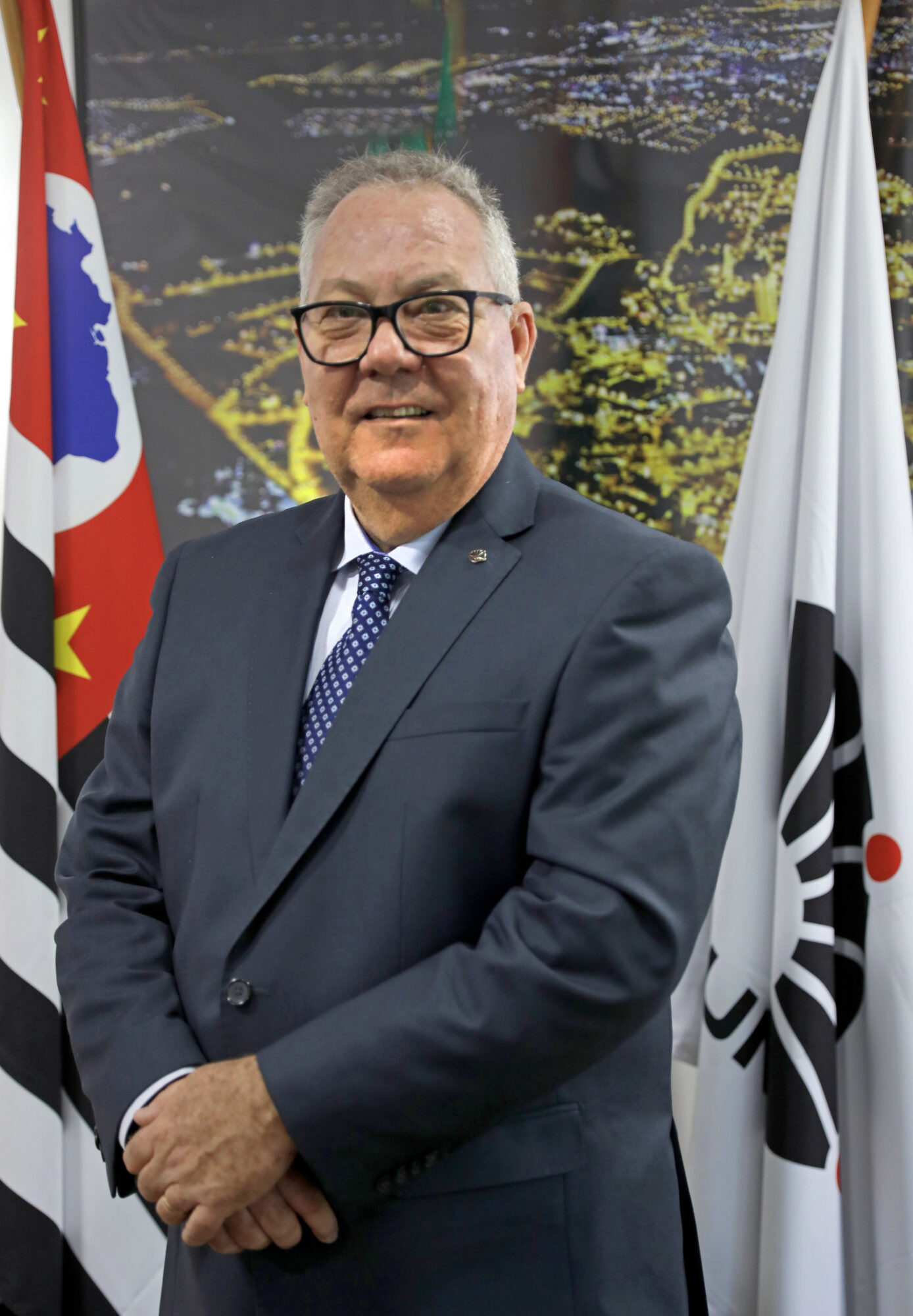 Reitor Paulo Cesar Montagner em pé entre as bandeiras do Estado de São Paulo, à esquerda, e da Unicamp, à direita, tendo às suas costas uma foto noturna do campus da Universidade.