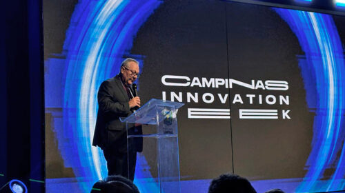 Reitor Paulo Cesar Montagner discursa de pé, em um palco, atrás de púlpito de acrílico transparente, tendo ao fundo um grande telão que exibe o logotipo da Campinas Innovation Week.