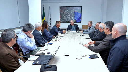Reitor Paulo César Montagner sentado à cabeceira de mesa de reuniões, tendo aos seus dois lados representantes da Unicamp e do Serviço Nacional de Aprendizagem Industrial (Senai), e, ao fundo, um quadro com uma fotografia aérea noturna do campus da Universidade em Campinas.