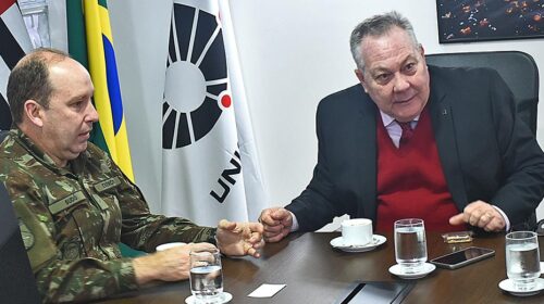 Reitor Paulo César Montagner sentado à cabeceira de mesa de reuniões, tendo à sua esquerda o general Santiago César França Budó, comandante da 11ª Brigada de Infantaria Mecanizada do Exército.