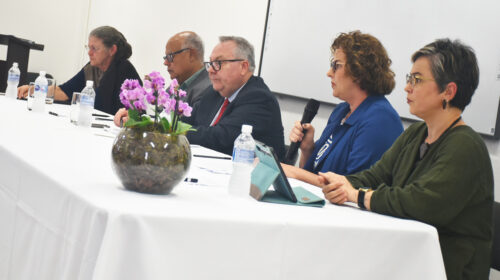 O reitor da Unicamp, Paulo Cesar Montagner, ocupa a posição central de mesa de autoridades composta por mais um homem e três mulheres. Uma delas, sentada ao lado dele, fala ao microfone.